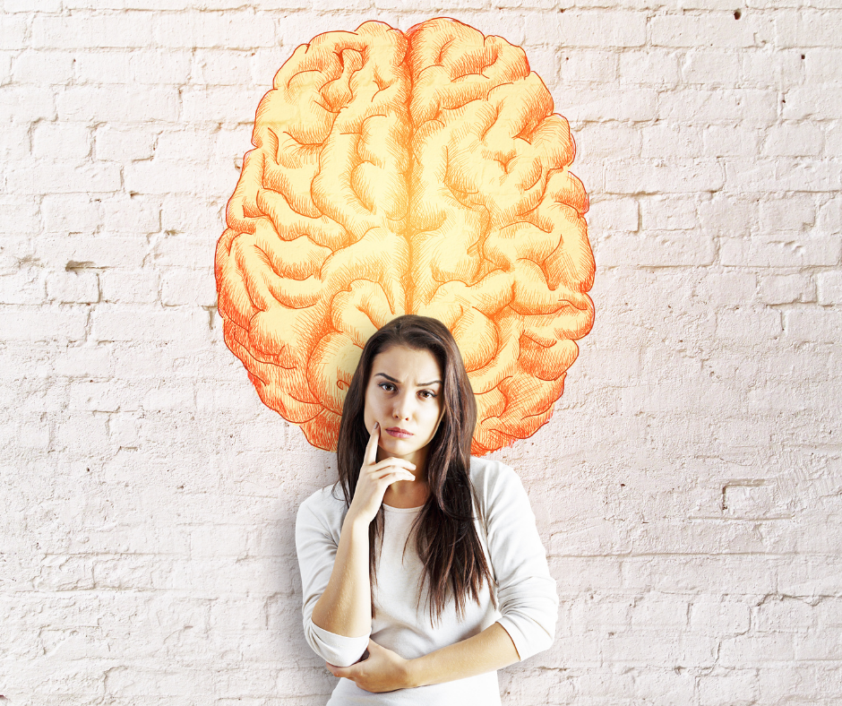 Zamyślona kobieta z przyłożonym palcem do policzka stojąca na tle ściany z rysunkiem mózgu